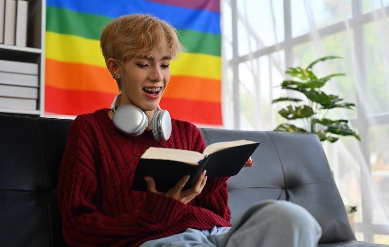 a student reads a book with a pride flag on the wall behind them